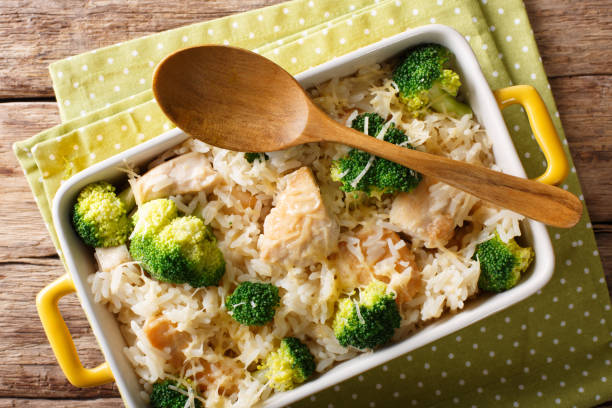 A casserole dish filled with rice, chicken pieces, and broccoli, accompanied by a wooden spoon.