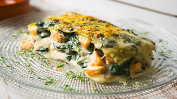 A serving of creamy spinach and salmon lasagna on a clear glass plate garnished with herbs.