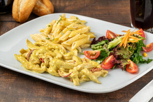 A plate of pasta with creamy pesto sauce, penne pasta, and a fresh garden salad with tomatoes and carrots