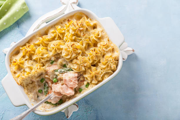 A creamy baked pasta dish with salmon, peas, and a golden-brown noodle topping in a white dish.