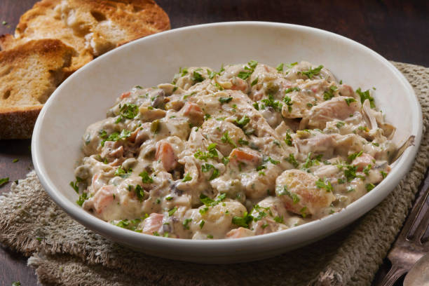 A creamy seafood dish with a variety of ingredients, garnished with parsley, served in a white bowl alongside toasted bread.