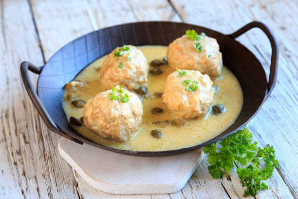 Four meatballs in a creamy sauce, garnished with herbs, served in a round cast iron pan.