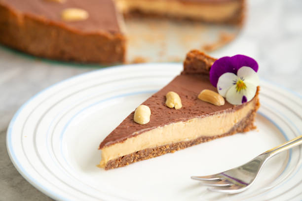 A slice of chocolate peanut butter cheesecake garnished with a flower and nuts on a white plate.