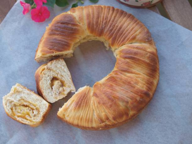 A round loaf of sweet bread with a golden-brown crust, partially sliced to reveal its soft, layered interior.