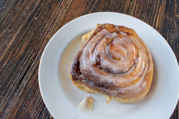 A freshly baked cinnamon roll with icing on a white plate