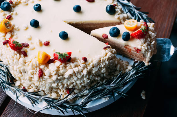 A delicious dessert cake with fruity toppings and a slice cut out, resting on a white plate adorned with rosemary branches.