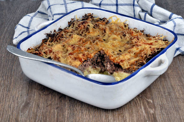 A baked casserole in a white dish with a blue rim, topped with golden brown cheese, sitting on a wooden surface.