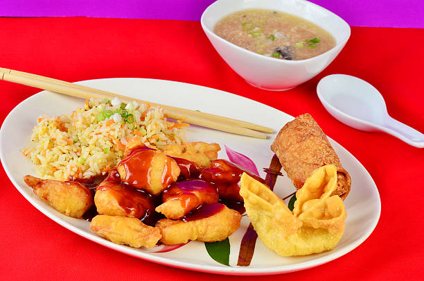 A plate of Chinese food including fried chicken with sweet sauce, fried rice, an egg roll, and wontons, accompanied by a bowl of soup.