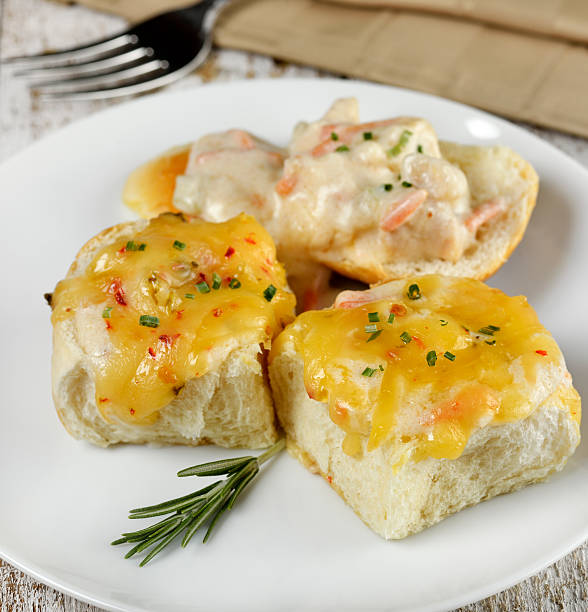 A plate of three baked rolls topped with cheese and creamy sauce, garnished with chives and a sprig of rosemary.