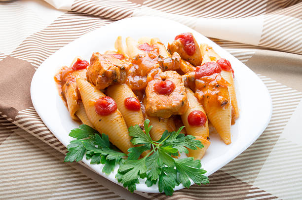 A plate of pasta shells with chicken, tomatoes, and parsley on a patterned tablecloth.