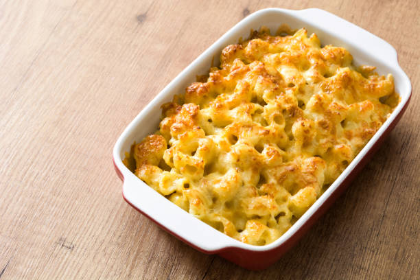 A baked dish of macaroni and cheese in a white and red casserole dish on a wooden surface.