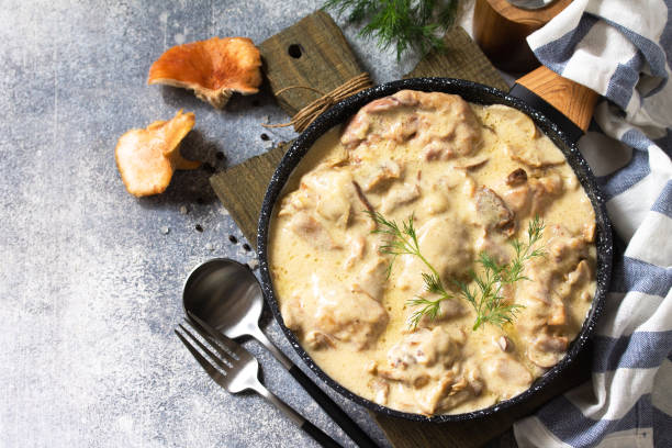 A plate of creamy mushroom dish served in a black skillet with herbs on top, accompanied by cutlery.