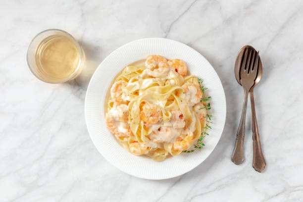 A plate of fettuccine pasta with shrimp in creamy sauce next to a glass of white wine.