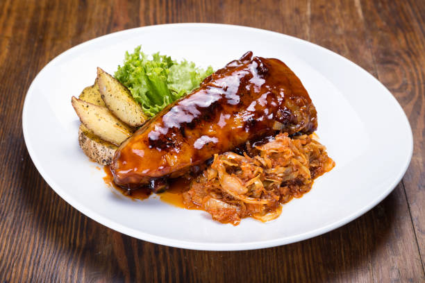 A plated dish featuring glazed chicken, spicy kimchi, potato wedges, and fresh greens on a white plate.