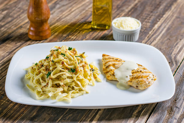 Grilled chicken with creamy sauce served alongside a bed of fettuccine pasta on a white plate.