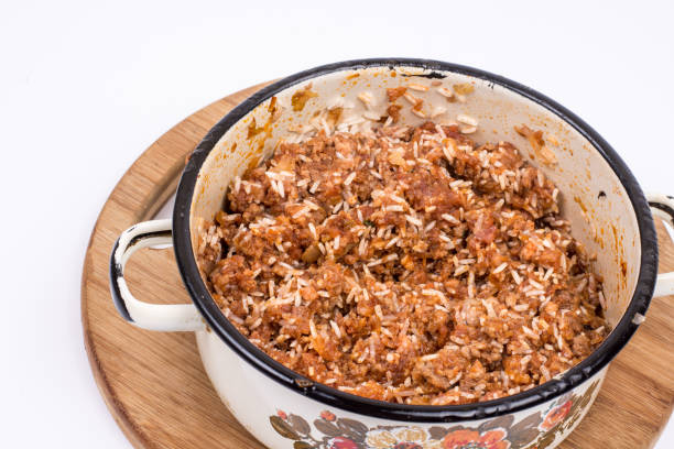 A pot filled with a mixture of rice and meat on a wooden cutting board.