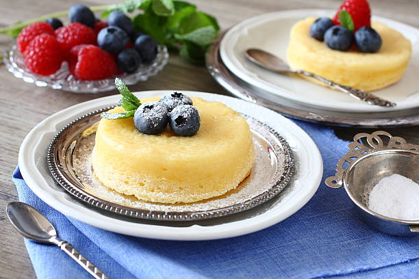 Two delicious mini cheesecakes topped with fresh blueberries and mint, served on silver plates alongside a bowl of powdered sugar and fresh raspberries.