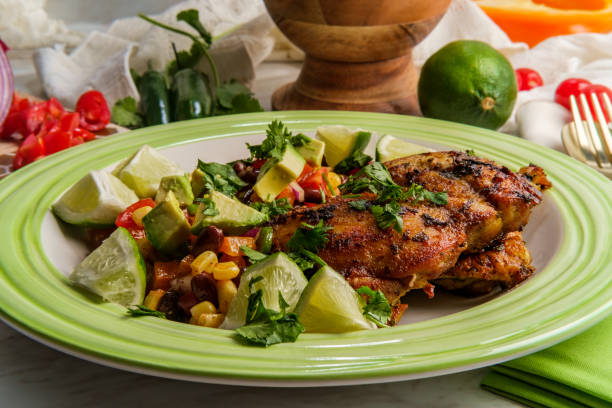 Grilled chicken served on a green plate with avocado, lime wedges, and a colorful salad.