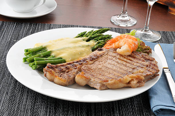 A delicious plate featuring a grilled steak, shrimp, asparagus, and a creamy sauce on a white plate.