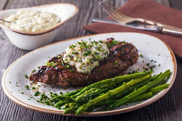 Grilled steak topped with creamy herb sauce served with asparagus on a rustic wooden table