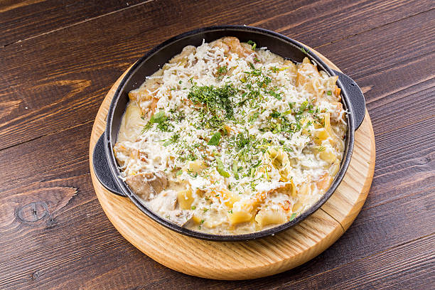 A delicious dish served in a black frying pan with cheesy pasta and herbs on a wooden plate.