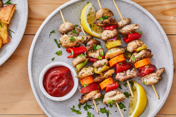 Delicious skewers of grilled chicken, mushrooms, and bell peppers on a plate with lemon and ketchup.