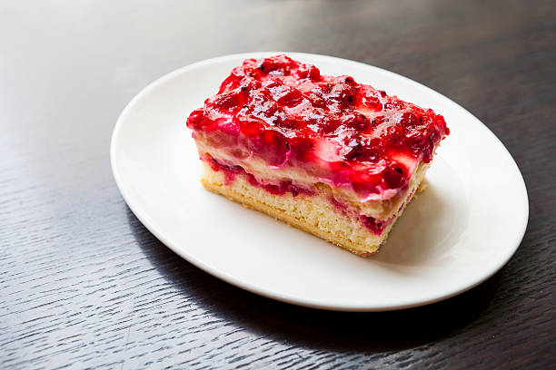 A slice of fruit cheesecake topped with red berry sauce on a white plate.