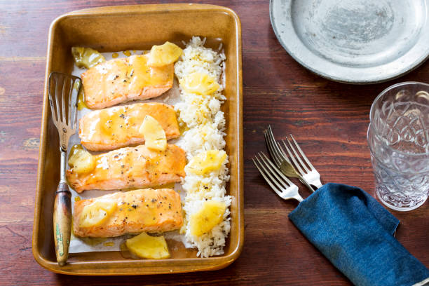 Baked salmon fillets with lemon sauce and rice on a wooden table.