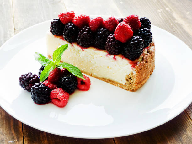 A slice of cheesecake topped with raspberries and blackberries, served on a white plate with fresh mint leaves.