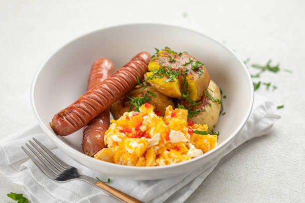 A bowl filled with scrambled eggs, sausages, and baked potatoes topped with herbs.