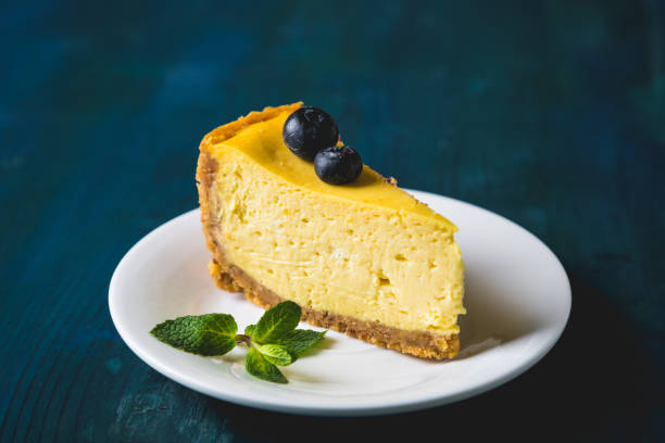 A slice of creamy cheesecake topped with blueberries and mint leaves on a white plate