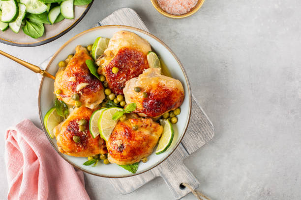 A plate of golden-brown chicken thighs garnished with lime slices and herbs, served with peas and a side of cucumber salad.