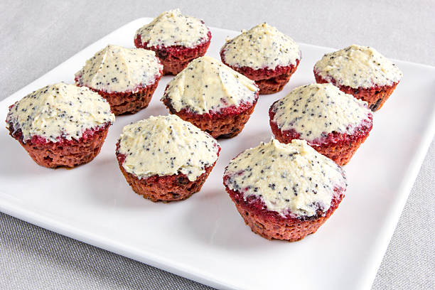 A plate of ten red velvet cupcakes with a cream cheese frosting on a light gray tablecloth.