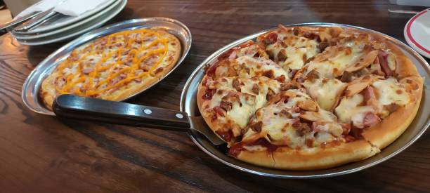 Two pizzas on metal plates, one topped with cheese and meats, the other with cheese and a signature drizzle.