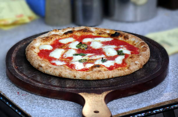 A freshly baked Margherita pizza topped with mozzarella cheese and basil leaves, sitting on a wooden pizza peel.