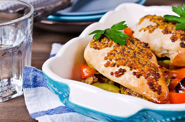 Baked chicken breasts with mustard glaze served on a bed of colorful vegetables in a blue dish.