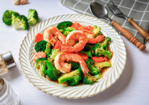 A plate of shrimp and broccoli stir-fry. Fresh shrimp are mixed with vibrant green broccoli and orange carrots in a savory sauce.