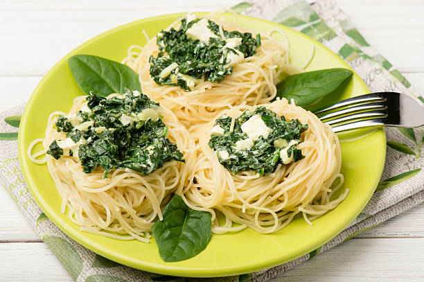 A plate of spaghetti garnished with spinach and creamy sauce.