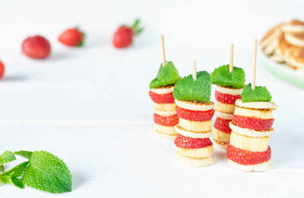 Healthy fruit skewers made of bananas and strawberries topped with mint leaves.