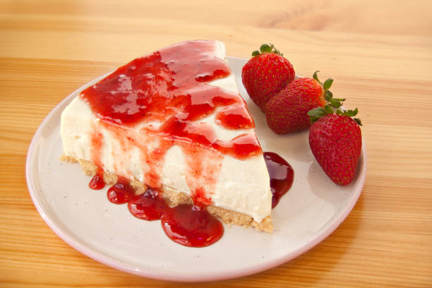 A slice of cheesecake topped with strawberry sauce on a plate, accompanied by fresh strawberries.