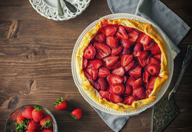 A delicious strawberry pie on a wooden table, surrounded by fresh strawberries.