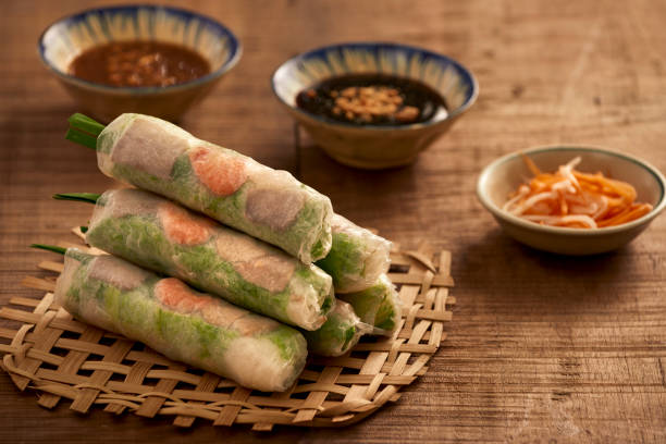 Four fresh Vietnamese spring rolls stacked on a woven bamboo tray with dipping sauces in the background.