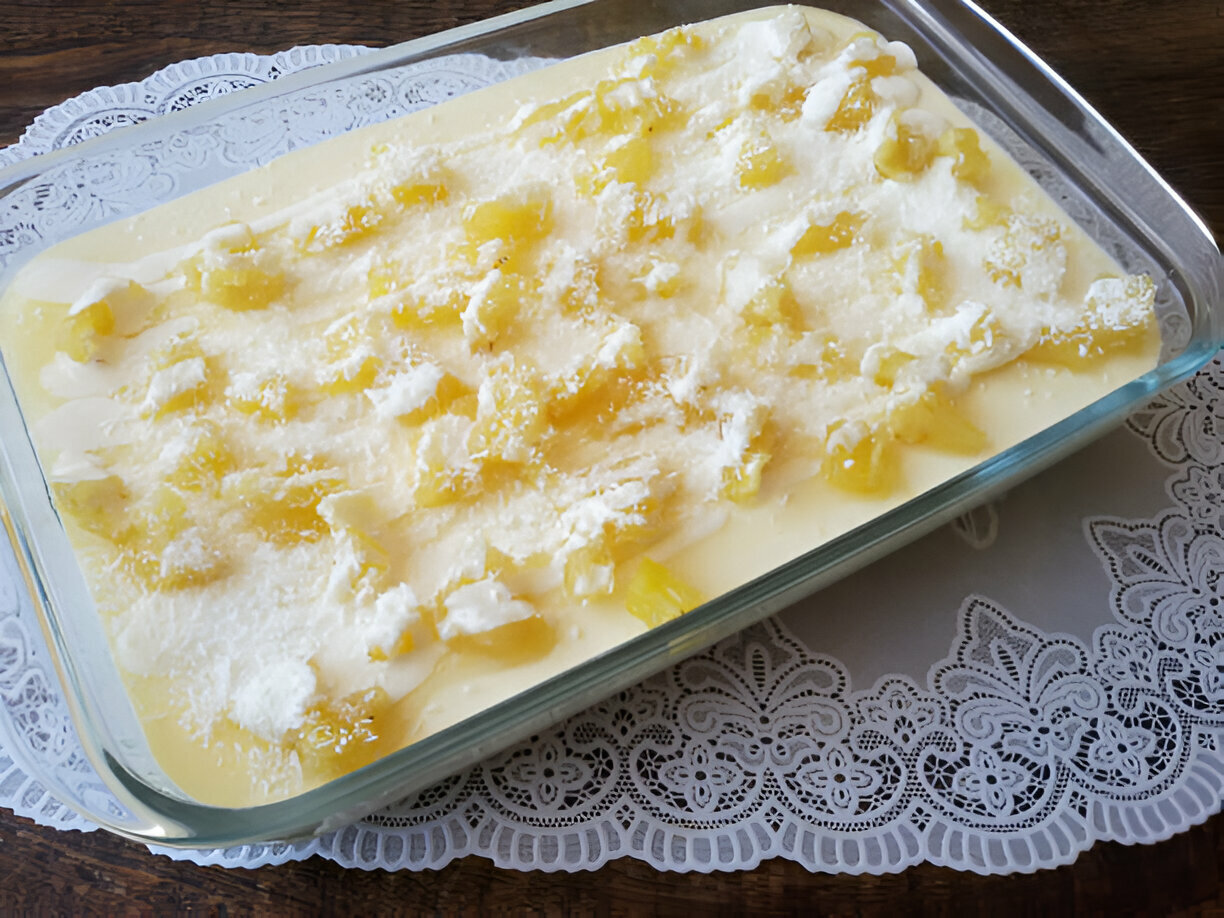 A delicious dessert featuring a creamy layer topped with pineapple chunks and grated coconut in a glass dish.