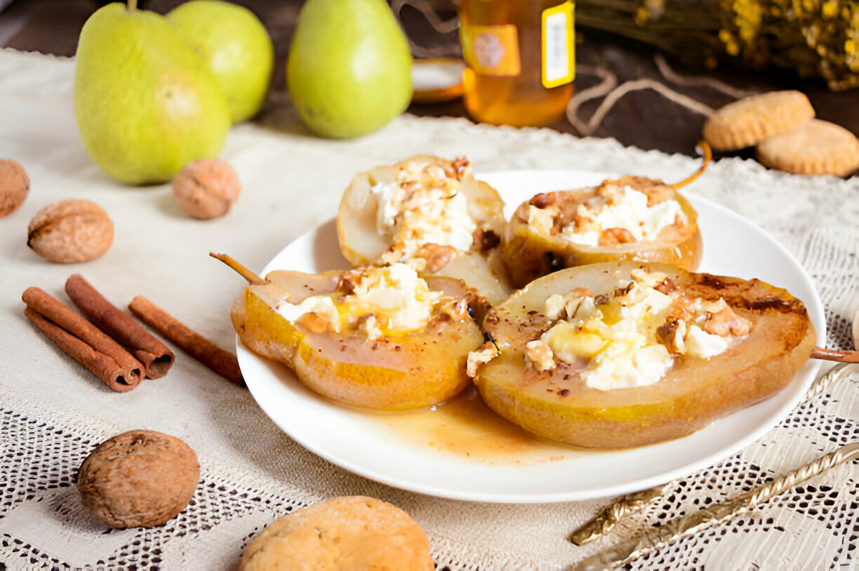 Baked pears topped with cheese and nuts on a white plate, with green pears and walnuts in the background