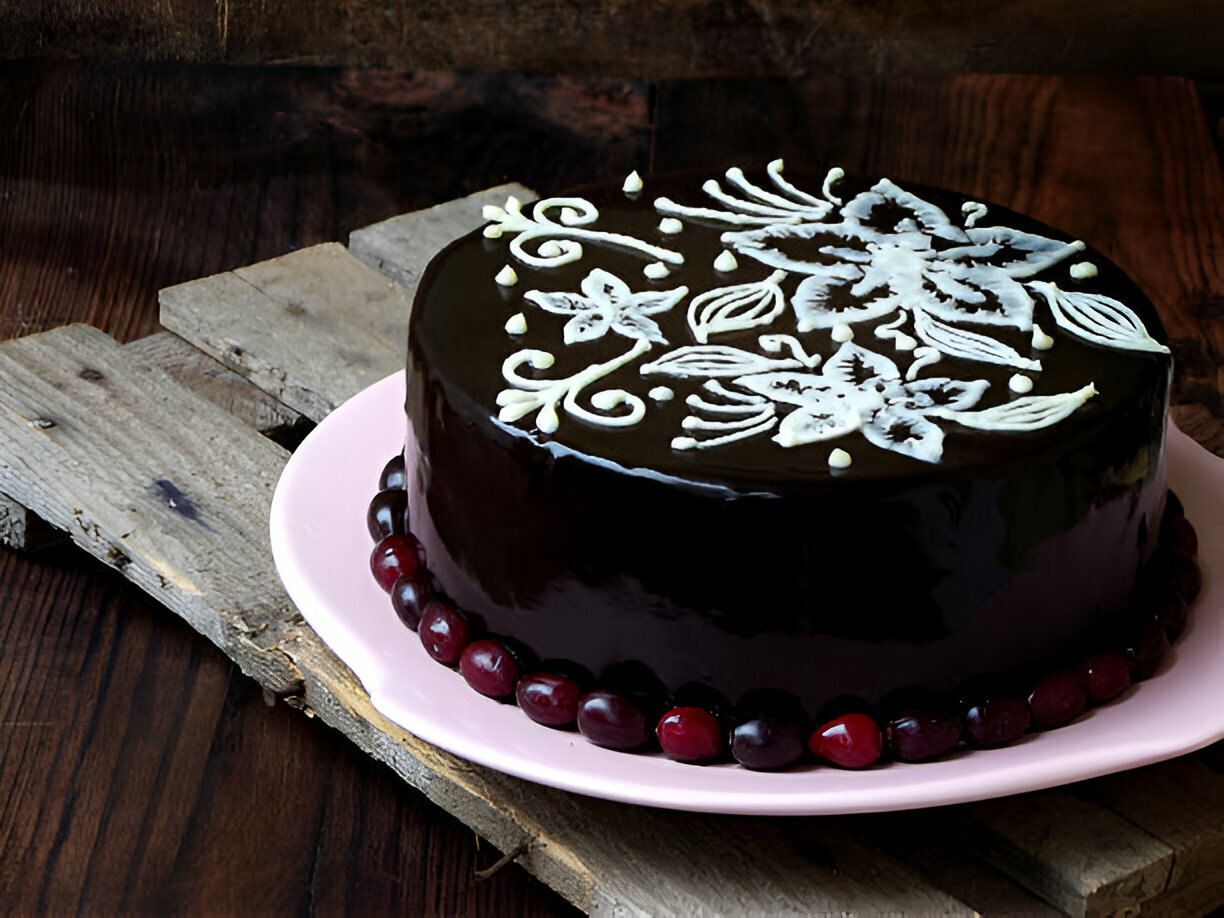 A beautifully decorated chocolate cake with floral designs on top, resting on a pink plate and surrounded by cherries.