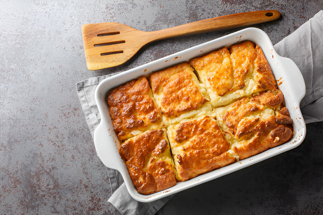 A freshly baked dish of golden brown dumplings in a white baking dish, with a wooden spatula nearby.