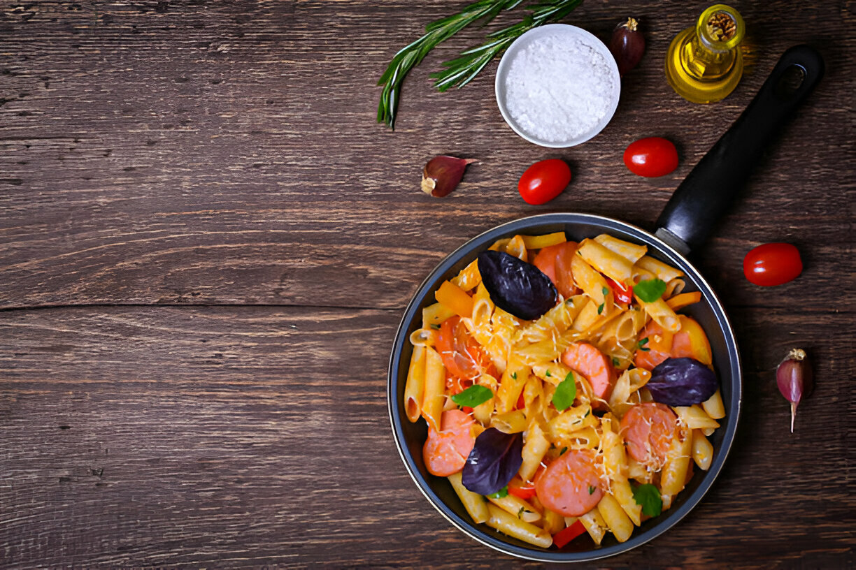 A colorful bowl of pasta with sausage, garnished with greens on a wooden table.