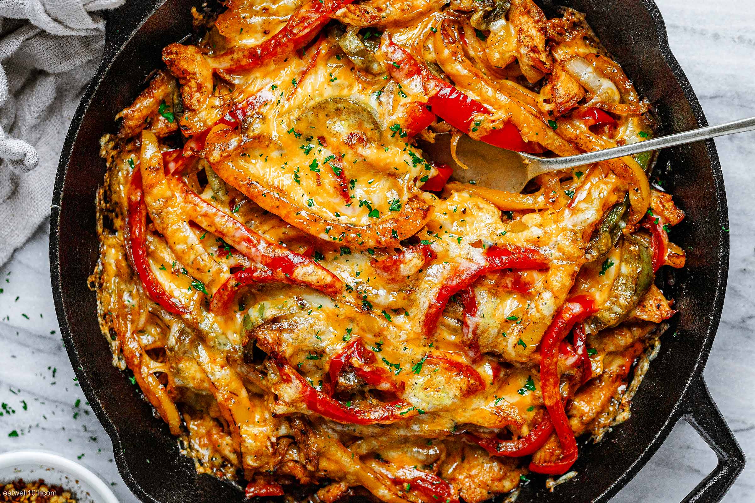 A delicious cheesy chicken dish topped with colorful bell peppers in a cast iron skillet.