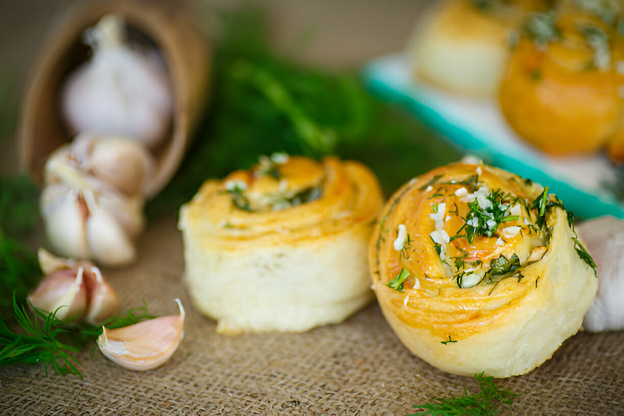 Delicious garlic rolls garnished with herbs and garlic cloves placed on burlap cloth.