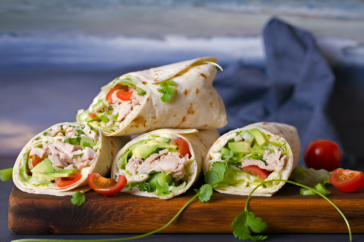 A stack of chicken wraps with fresh vegetables on a wooden cutting board.